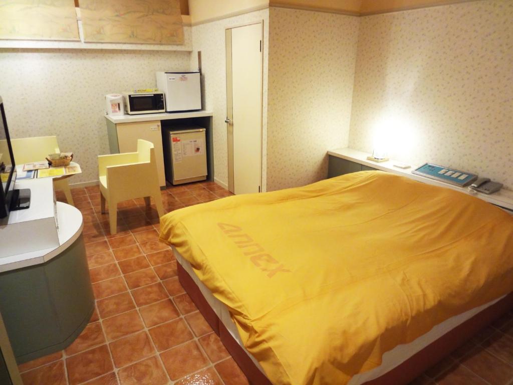 une chambre d'hôtel avec un lit jaune et une cuisine dans l'établissement アネックスたまゆ 大人専用, à Matsue