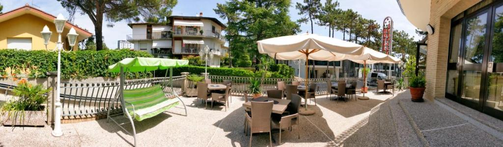 un patio avec tables, chaises et parasols dans l'établissement Hotel Acapulco, à Lignano Sabbiadoro