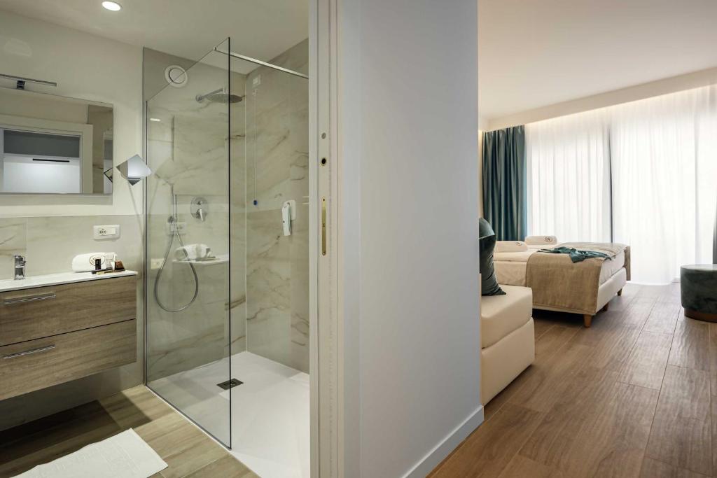 une salle de bain avec une douche et un lavabo et un lit dans l'établissement Hotel Astoria, à Bibione