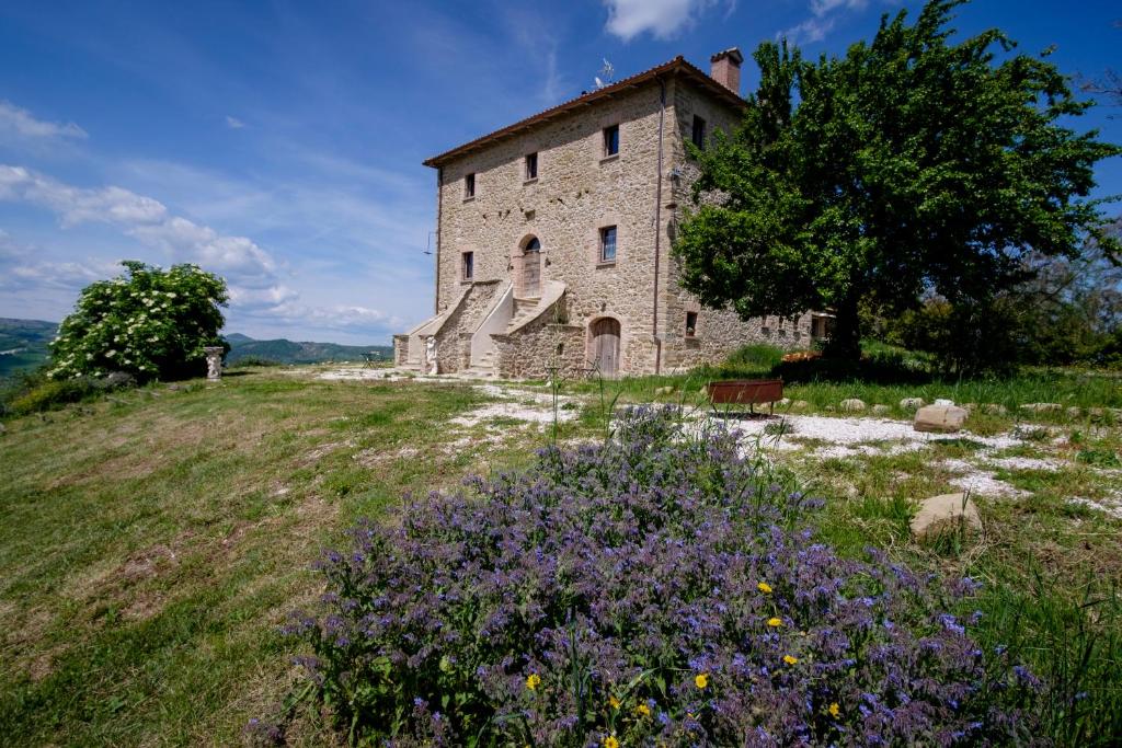 un vieux bâtiment en pierre sur une colline avec des fleurs violettes dans l'établissement Palazzo Serre - Natura & Piscina, à San Leo