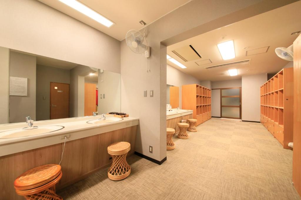 une grande salle de bains avec deux lavabos et une rangée de tabourets dans l'établissement Hotel Kamogawaso, à Takekara