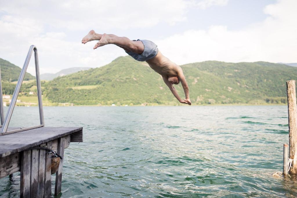un homme sautant dans l'eau à partir d'un quai dans l'établissement Lake Spa Hotel SEELEITEN, à Caldaro