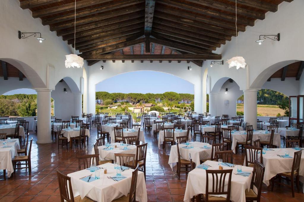 une salle de banquet avec des tables et des chaises blanches dans l'établissement Cala Luas Resort, à Cardedu