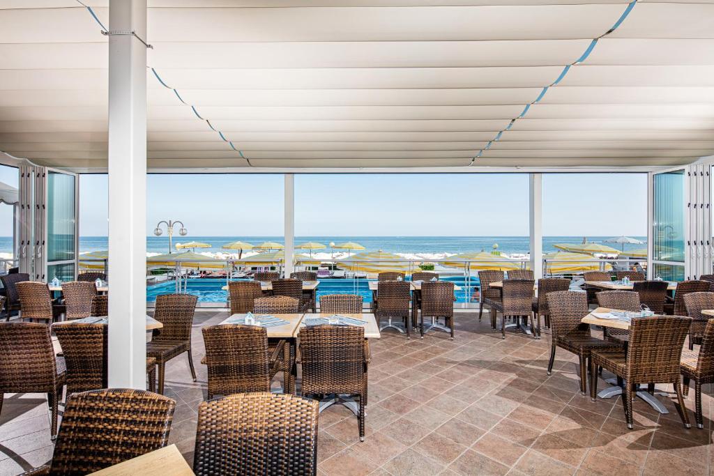 un restaurant avec des tables et des chaises et une vue sur l'océan dans l'établissement Hotel Capitol, à Lido di Jesolo