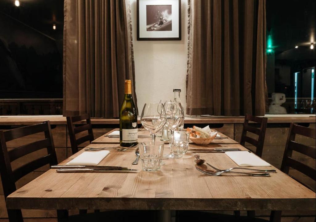 - une table en bois avec une bouteille de vin et des verres dans l'établissement Langley Hôtel Le Petit Prince, à L'Alpe-d'Huez