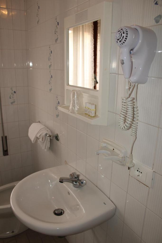 une salle de bain avec un lavabo et un sèche-cheveux au mur dans l'établissement Hotel Caravel, à Sottomarina