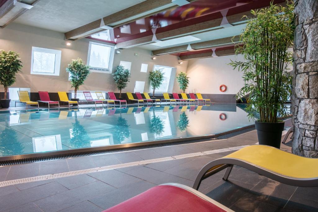 une piscine avec des chaises colorées dans un bâtiment dans l'établissement CGH Résidence Boutique Le Centaure, à Flaine