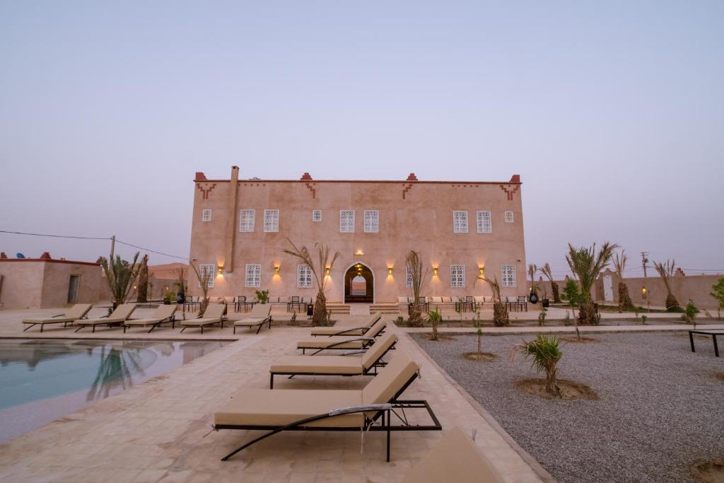 - un bâtiment avec une piscine et des bancs devant dans l'établissement Riad Chebbi, à Merzouga