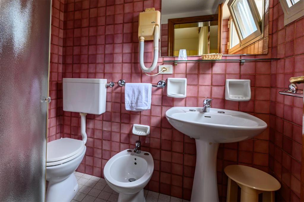 une salle de bain carrelée rouge avec toilettes et lavabo dans l'établissement Hotel San Marco, à Lido di Jesolo
