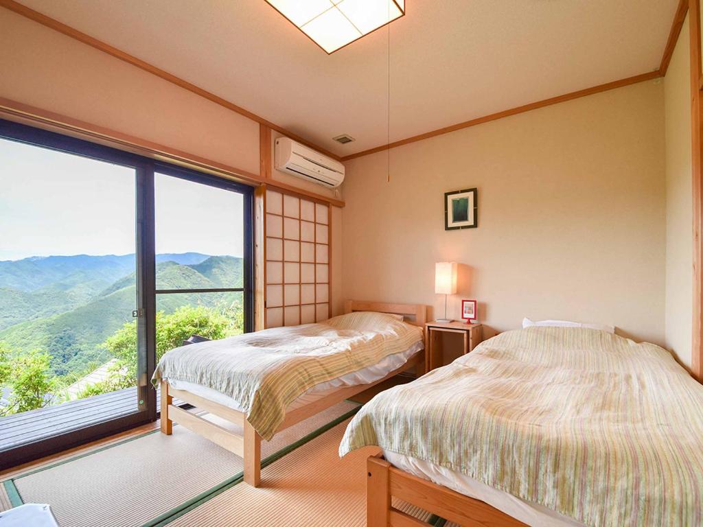 deux lits dans une chambre avec une grande fenêtre dans l'établissement Kirinosato Takahara, à Tanabe
