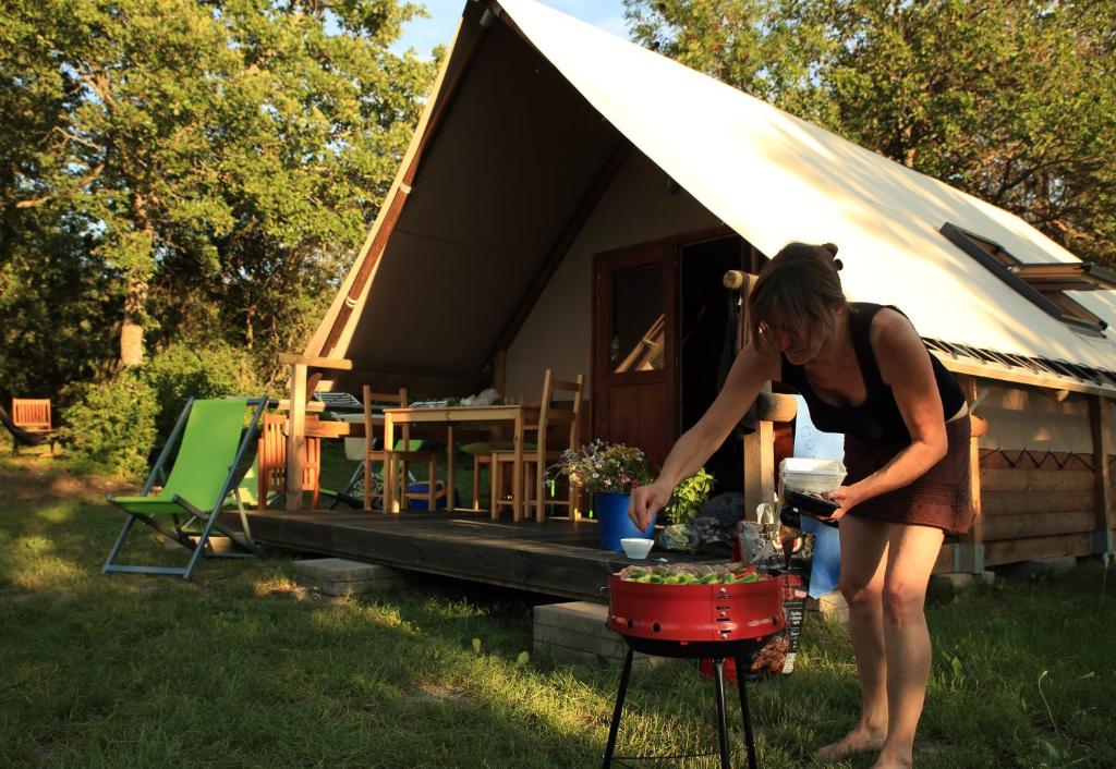 une femme préparant de la nourriture devant une tente dans l'établissement Camping le Petit Liou Sites & Paysages, à Baratier