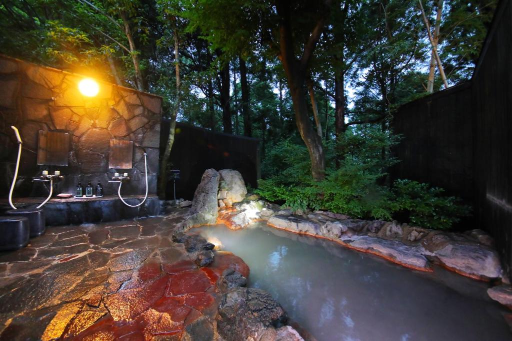 un bain à remous dans un jardin avec un mur en pierre dans l'établissement Sakura Sakura Onsen, à Kirishima