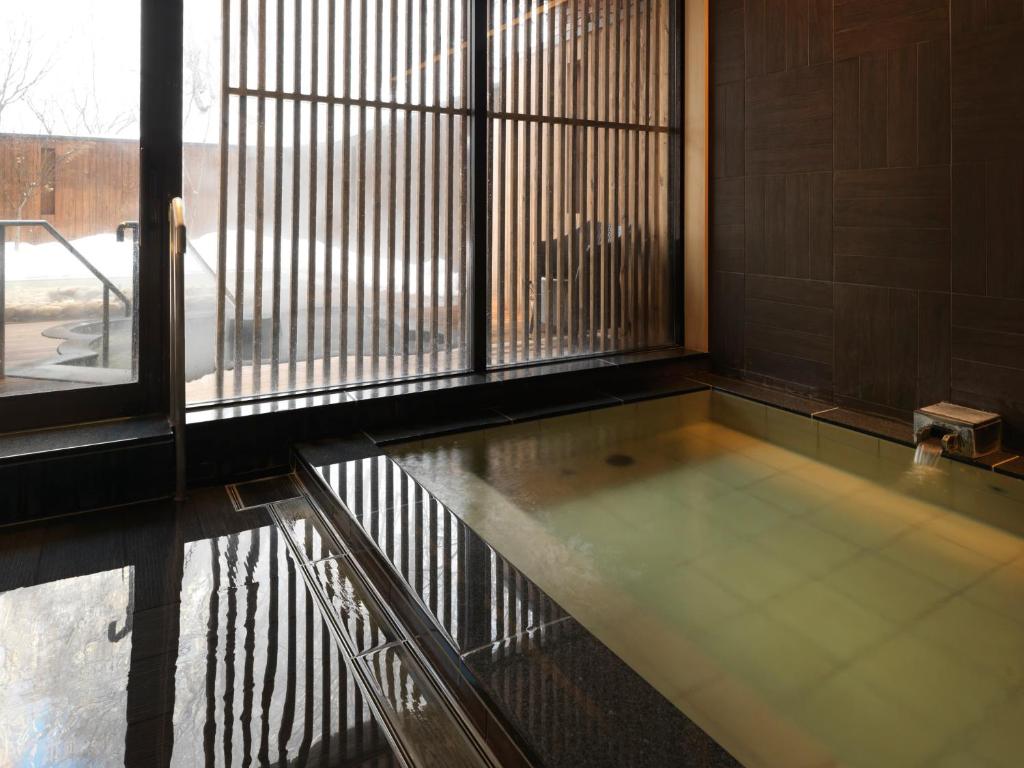 une baignoire dans une pièce avec une grande fenêtre dans l'établissement Niseko Konbu Onsen Tsuruga Moku-no-sho, à Niseko