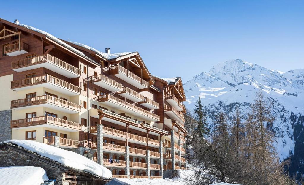 un bâtiment dans la neige avec des montagnes en arrière-plan dans l'établissement Résidence Club mmv L'Étoile des Cimes ****, à Sainte-Foy-Tarentaise