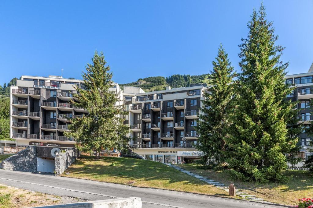 un immeuble d'appartements avec des arbres devant une route dans l'établissement Résidence Pierre & Vacances La Forêt, à Flaine
