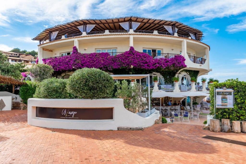 un bâtiment avec des fleurs violettes devant lui dans l'établissement Club Hotel Baja Sardinia, à Baja Sardinia