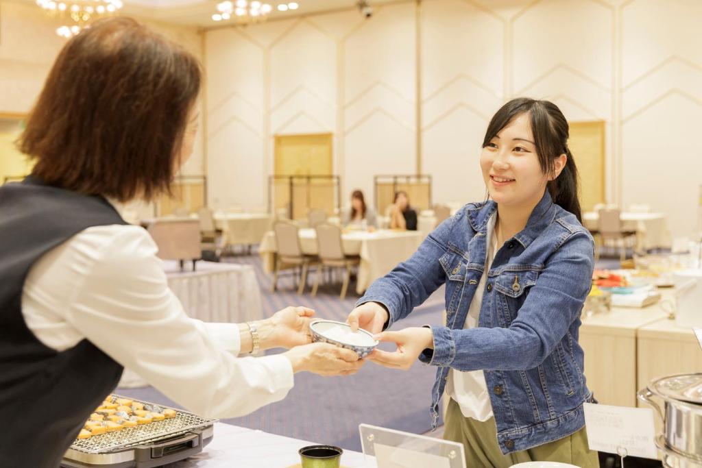 Une femme qui remet à une autre femme une assiette de nourriture dans l'établissement Hotel Shion, à Morioka 90 autres photos