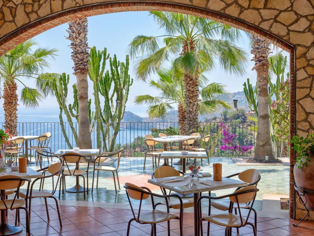 un restaurant avec des tables, des chaises et des palmiers dans l'établissement Hotel Olimpo le Terrazze, à Letojanni