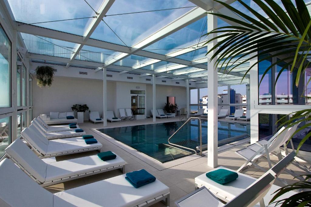 une piscine intérieure avec des chaises blanches et une piscine dans l'établissement Hotel Florida, à Lignano Sabbiadoro