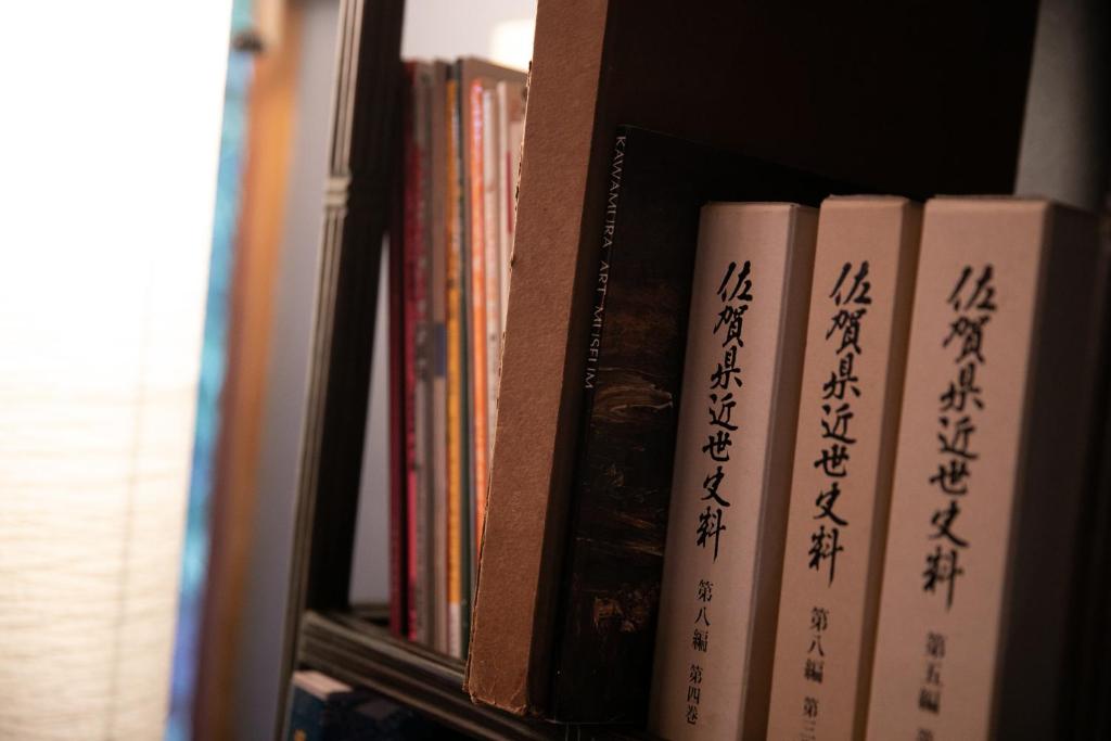 une rangée de livres sur une étagère avec écriture sur eux dans l'établissement Ryokan Wataya, à Karatsu