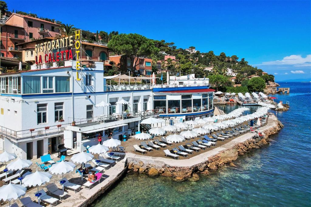 un hôtel avec des chaises et des parasols dans l'eau dans l'établissement Hotel La Caletta, à Porto Santo Stefano