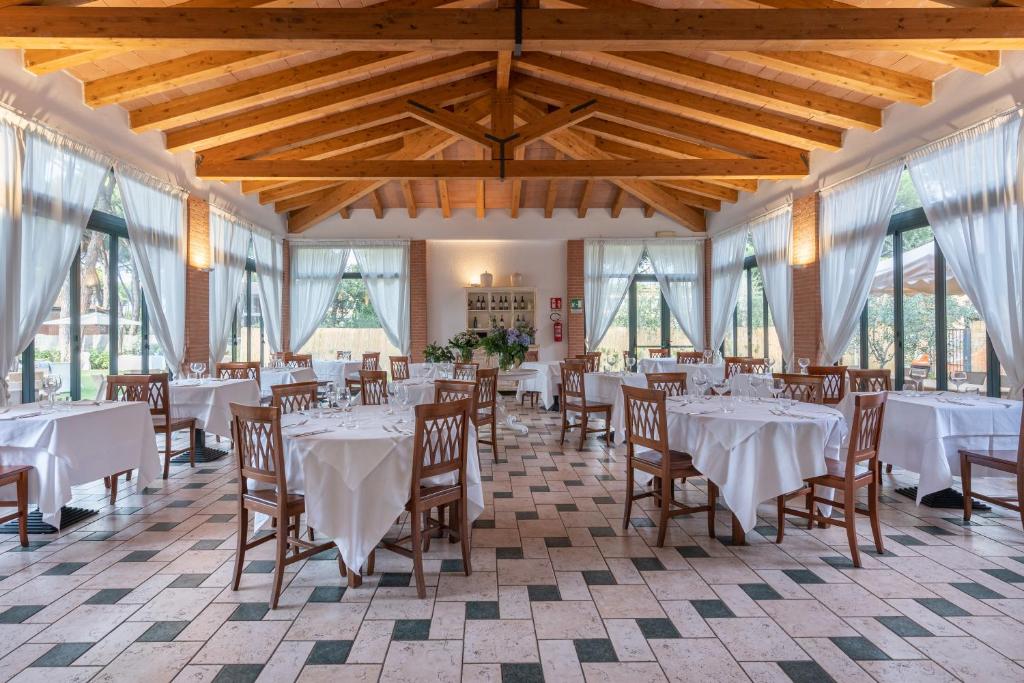 une salle à manger avec des tables et des chaises blanches et des fenêtres dans l'établissement Ricci Hotel - Marina di Grosseto, à Marina di Grosseto