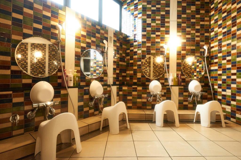 une rangée d'urinoirs dans une salle de bain avec des miroirs dans l'établissement 層雲峡温泉 ホテル雲井, à Kamikawa