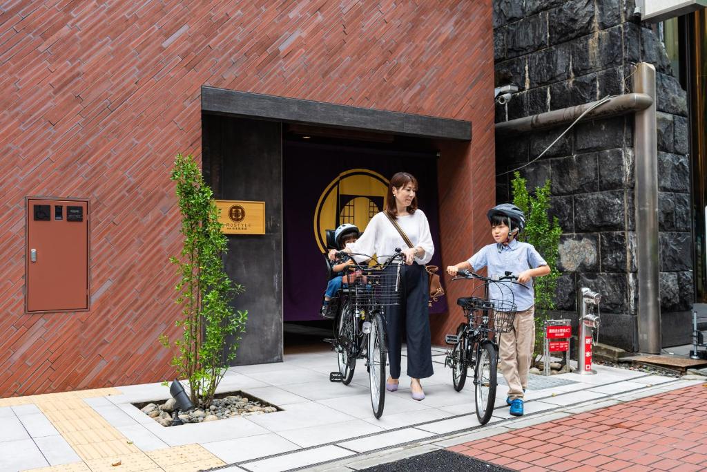 Une femme et deux enfants montent des vélos à l'extérieur d'un bâtiment dans l'établissement PROSTYLE Ryokan Yokohama Bashamichi, à Yokohama