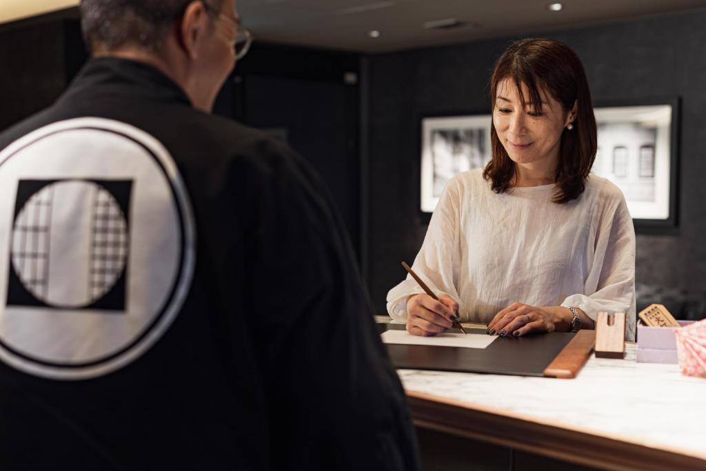 un homme et une femme écrivant sur un papier dans l'établissement PROSTYLE Ryokan Yokohama Bashamichi, à Yokohama