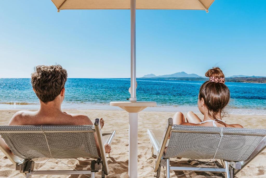 un homme et une femme assis sur des chaises sur la plage dans l'établissement Hotel Club Saraceno - Bovis Hotels, à Àrbatax