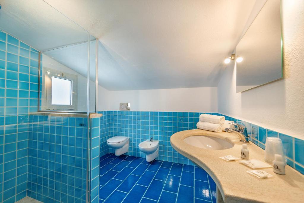 La salle de bains est pourvue de carrelage bleu, d'un lavabo et de toilettes. dans l'établissement Hotel Le Mimose, à San Teodoro 32 autres photos