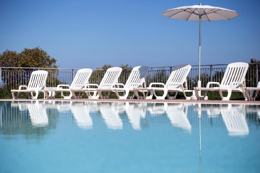 un groupe de chaises blanches et un parasol à côté d'une piscine dans l'établissement Happy Days, à Capo Vaticano