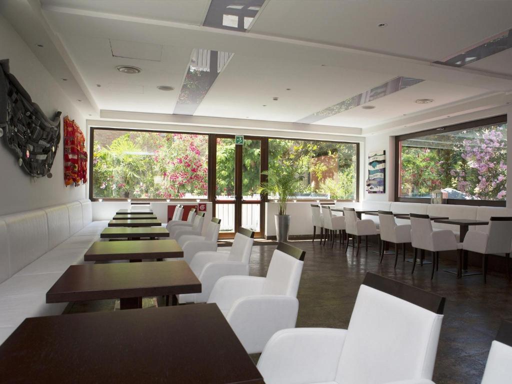 un restaurant avec des chaises et des tables blanches et des fenêtres dans l'établissement Hotel Villa Pannonia, sur le Lido de Venise