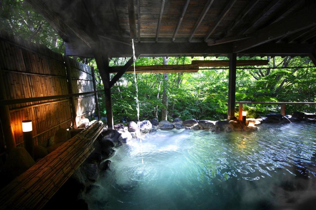 - une piscine avec des rochers et de l'eau dans un bâtiment dans l'établissement Takamiya Hotel Bonari no Mori, à Inawashiro