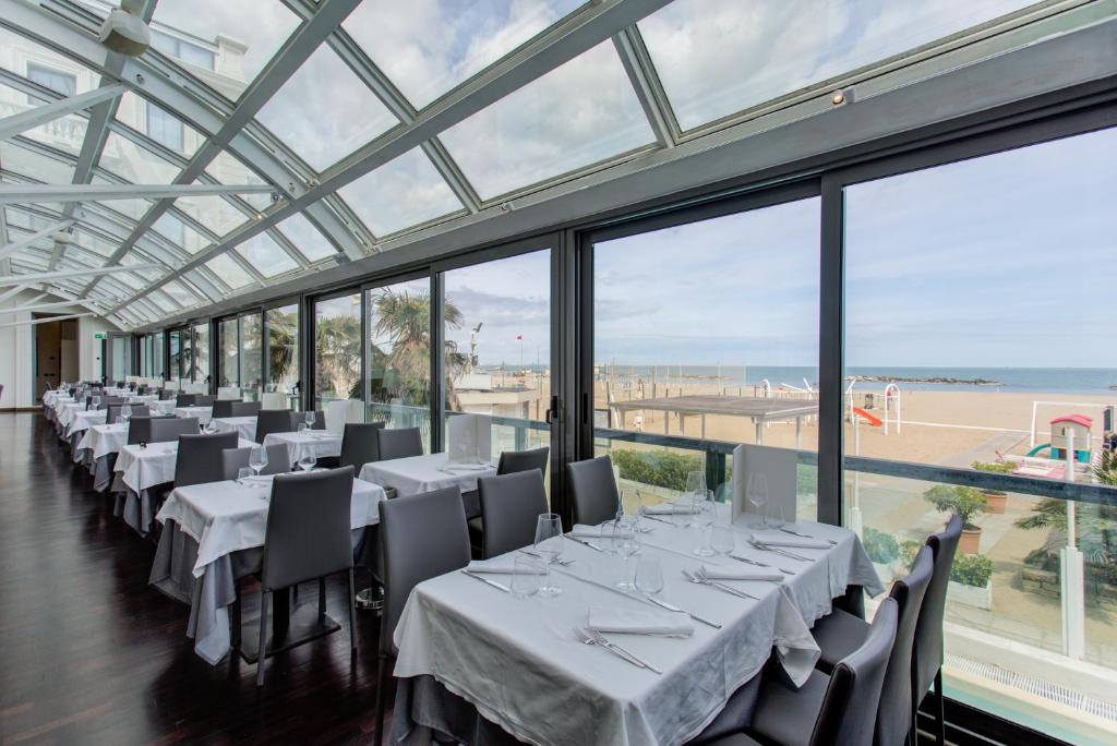 une salle à manger avec des tables et des chaises blanches et des fenêtres dans l'établissement Kursaal Hotel, à Cattolica