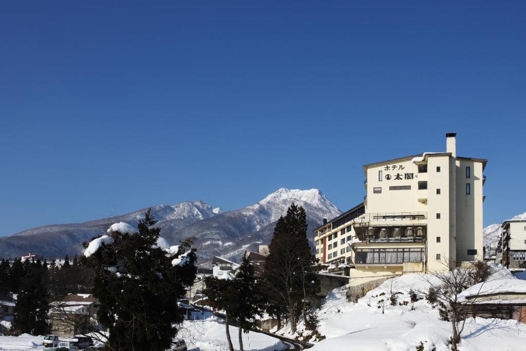 un bâtiment dans la neige avec des montagnes en arrière-plan dans l'établissement Hotel Taiko, à Myōkō