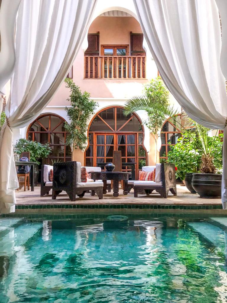 - une piscine en face d'une maison avec des rideaux blancs dans l'établissement Riad Selouane, à Marrakech