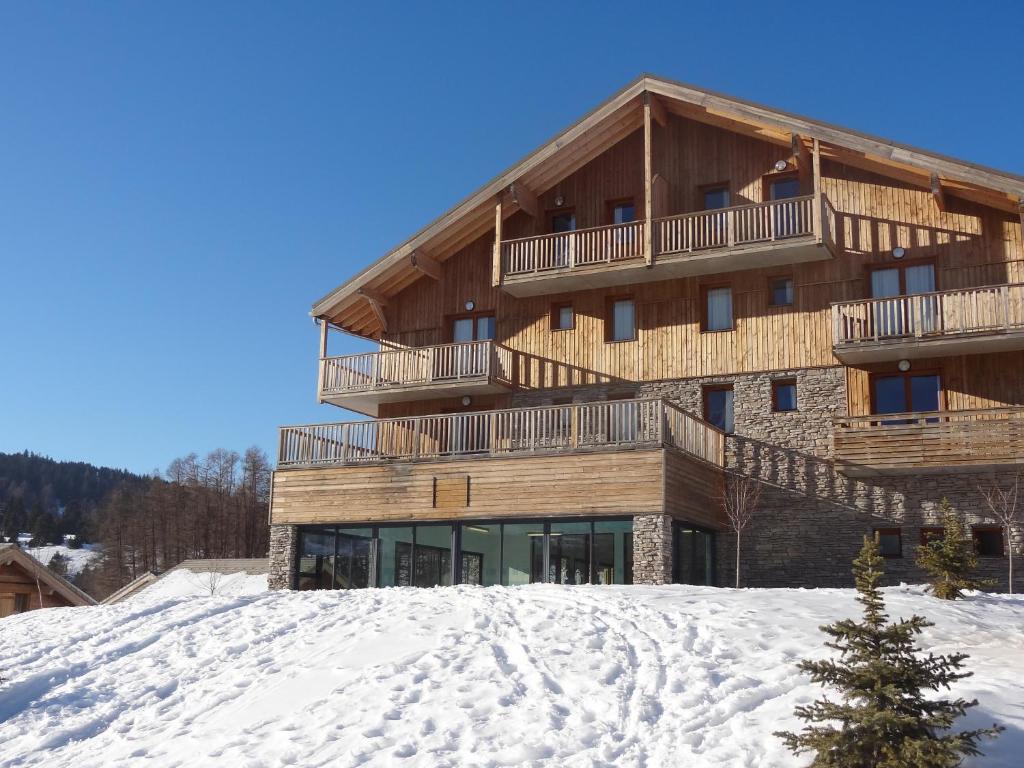 un grand bâtiment en bois au sommet d'une piste enneigée dans l'établissement Residence Le Hameau du Puy by Actisource, à Saint-Étienne-en-Dévoluy