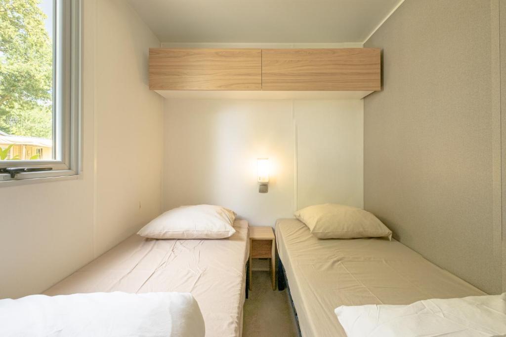 deux lits dans une petite pièce avec une fenêtre dans l'établissement Marino Mobilhomes, à Grimaud