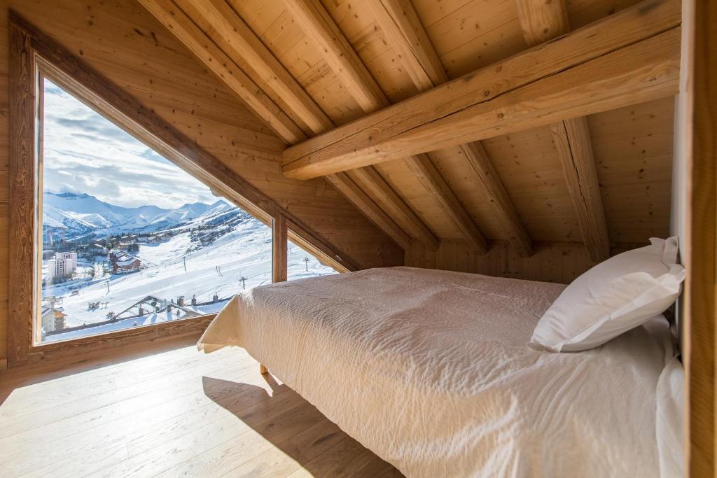 un lit dans une chambre avec une grande fenêtre dans l'établissement ODYSSEE B301 Duplex mansarde sur les pistes, vue panoramique, à La Toussuire