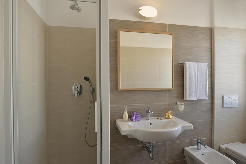 une salle de bain avec un lavabo, un miroir et une douche dans l'établissement Hotel Tiberius, à Rimini
