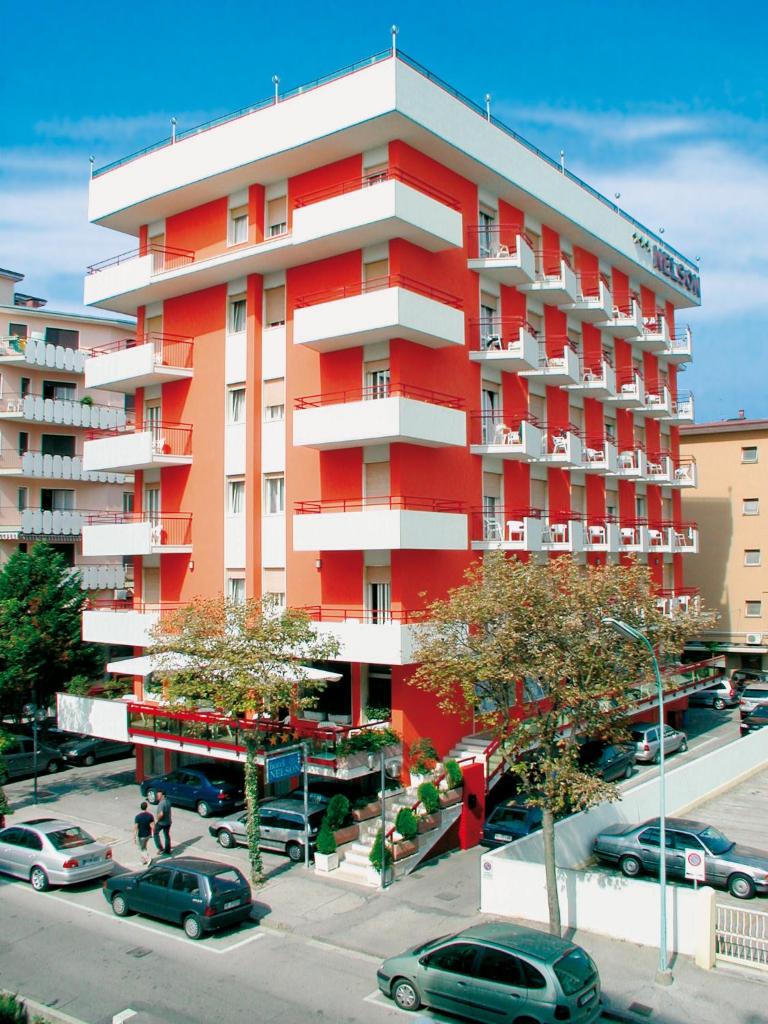un bâtiment rouge avec des voitures garées dans un parking dans l'établissement Hotel Nelson, à Lido di Jesolo
