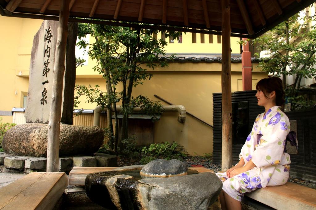 une femme en kimono assise à côté d'une fontaine dans l'établissement Ougiya Ryokan, à Toyooka