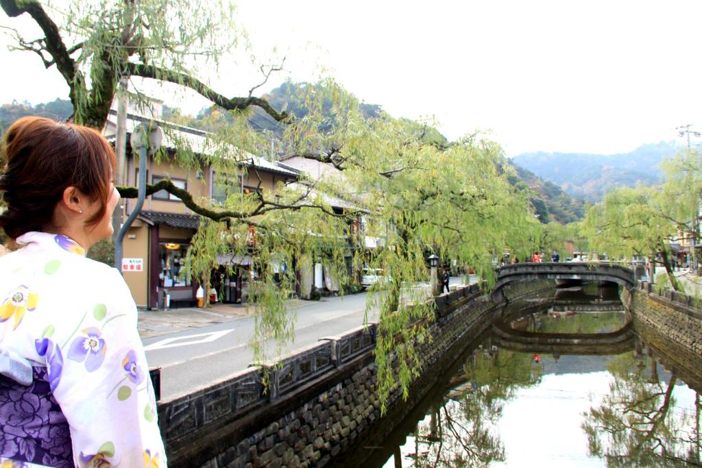une femme debout à côté d'une rivière avec un pont dans l'établissement Ougiya Ryokan, à Toyooka
