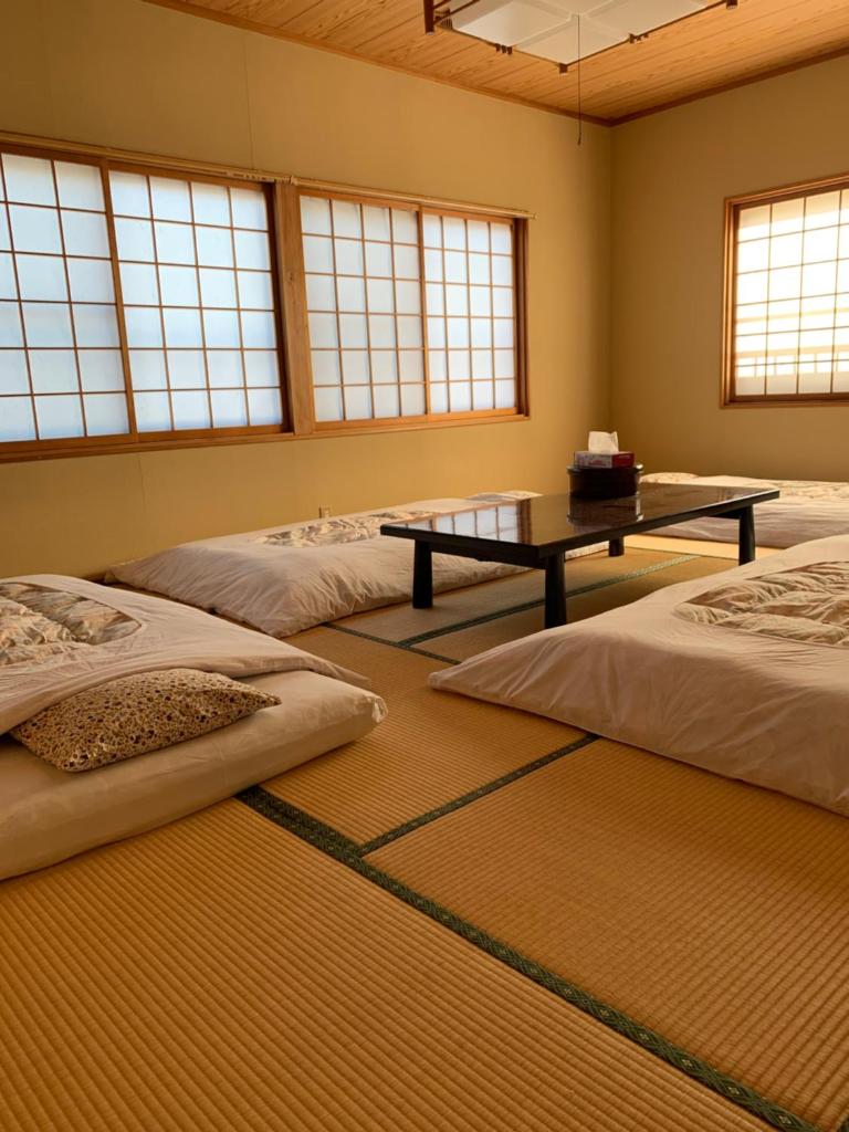 une chambre avec trois lits et une table dedans dans l'établissement たから温泉民宿 Gem Onsen Stay, à Sakaimura