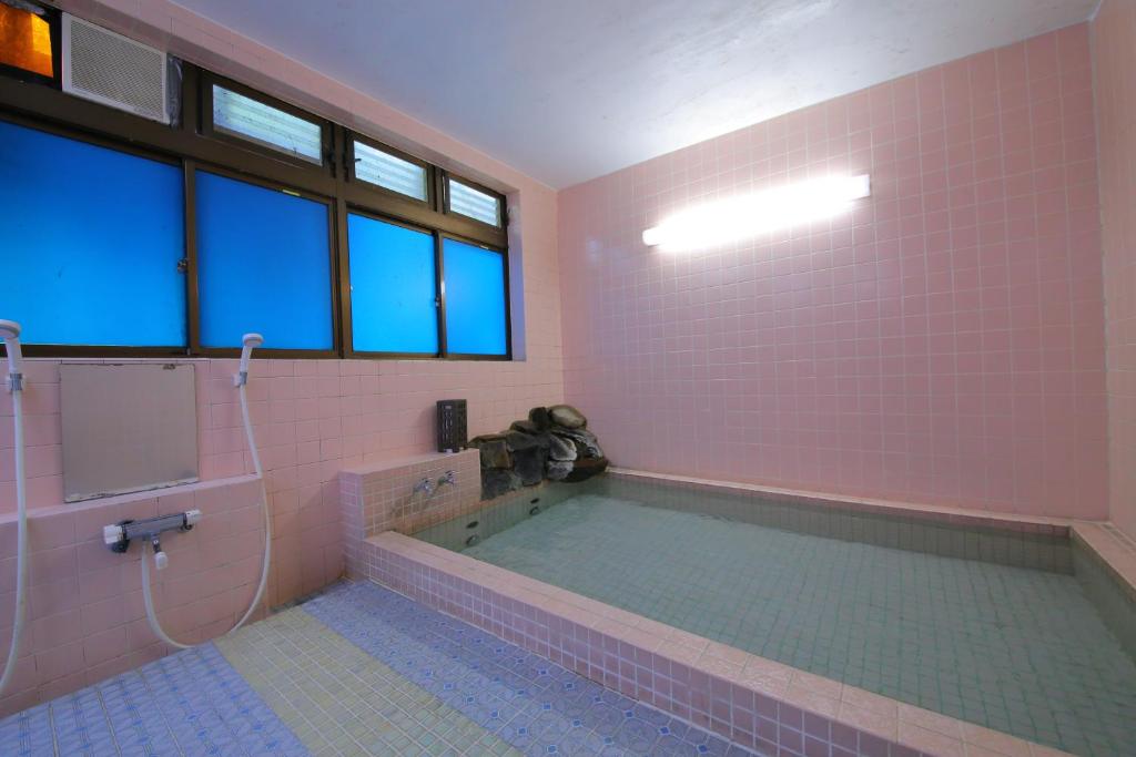 La salle de bains est pourvue d'une grande baignoire avec du carrelage rose. dans l'établissement Lake Side Hotel Minatoya, à Inawashiro