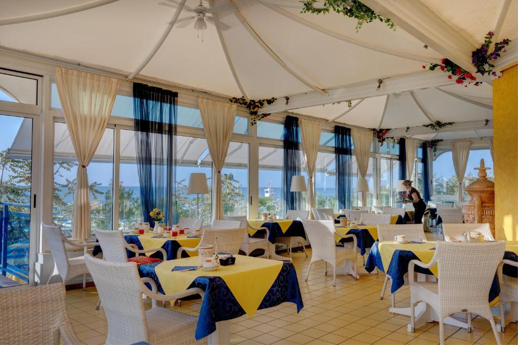 un restaurant avec des tables et des chaises blanches et des fenêtres dans l'établissement Hotel Napoleon, à Lido di Jesolo 156 autres photos