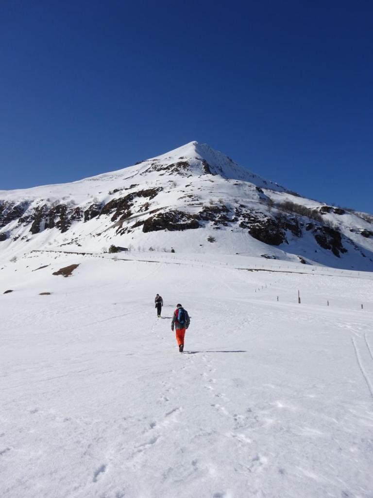 deux personnes marchant dans la neige devant une montagne dans l'établissement BIENVENUE AU LIORAN, à Le Lioran
