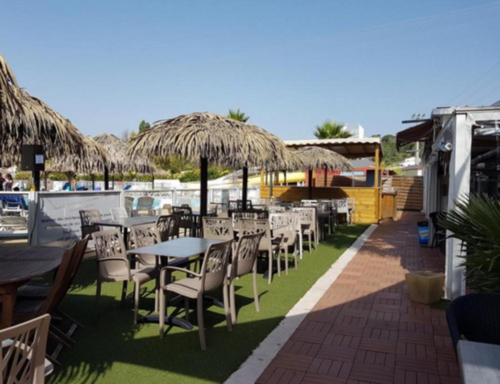 une rangée de tables et de chaises avec parasols en paille dans l'établissement GRAND MOBILEHOME PROCHE COMMODITE FO10, à Fréjus