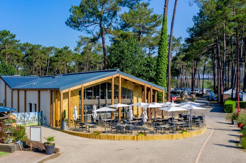 un bâtiment avec des tables et des parasols devant lui dans l'établissement Les Dunes de Contis, à Saint-Julien-en-Born